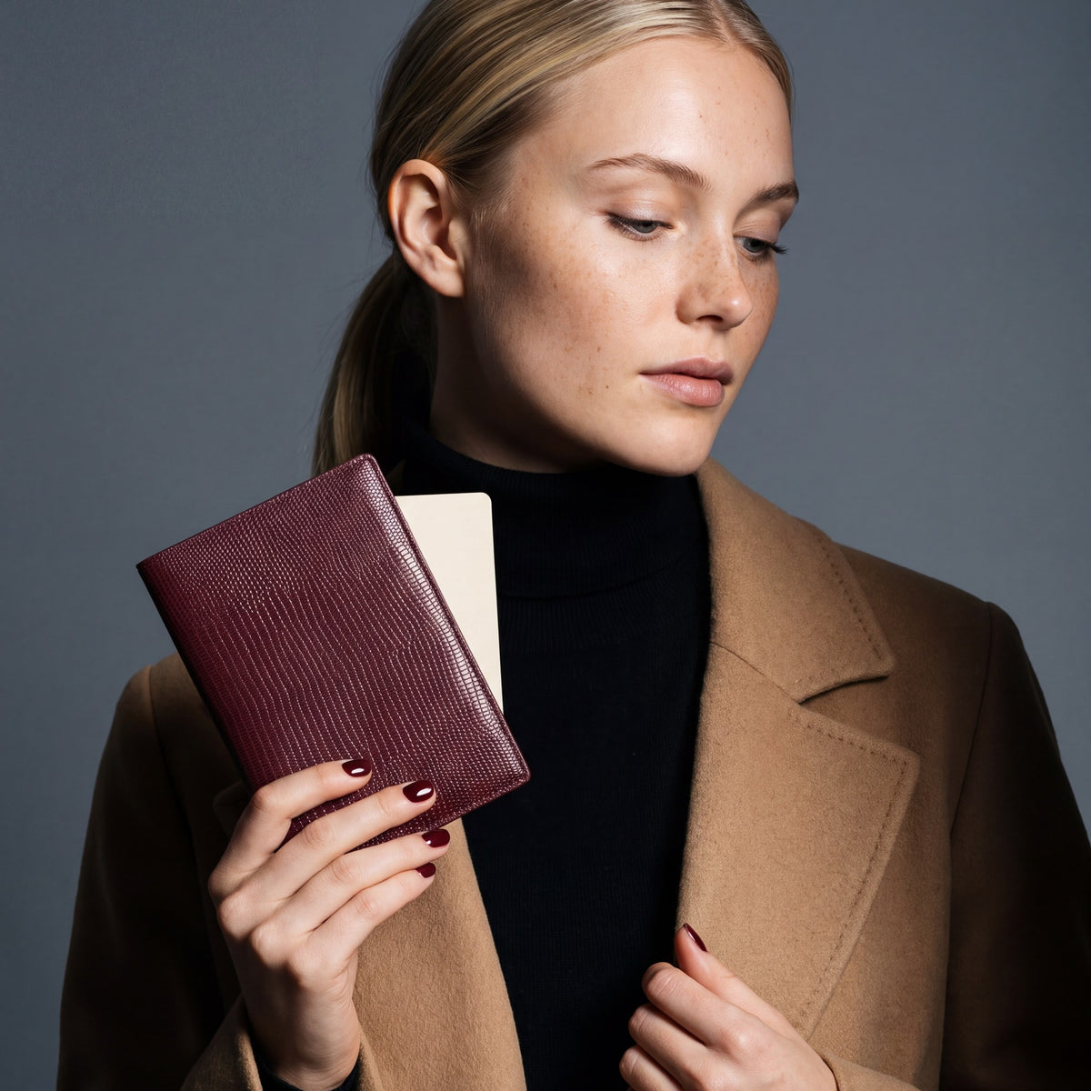 Woman holding a burgundy lizard-embossed leather passport holder by GENTCREATE with a blank card tucked in