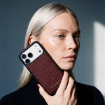 امرأة تمسك جرابًا عنابيًا لهاتف iPhone 18 Pro Max من جلد عجل بنقش موجي بارز من GENTCREATE بجانب وجهها تحت ضوء النافذة