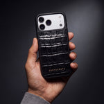 Man's hand holding a black glossy crocodile-embossed calfskin iPhone 18 Pro Max case by GENTCREATE in a dark studio