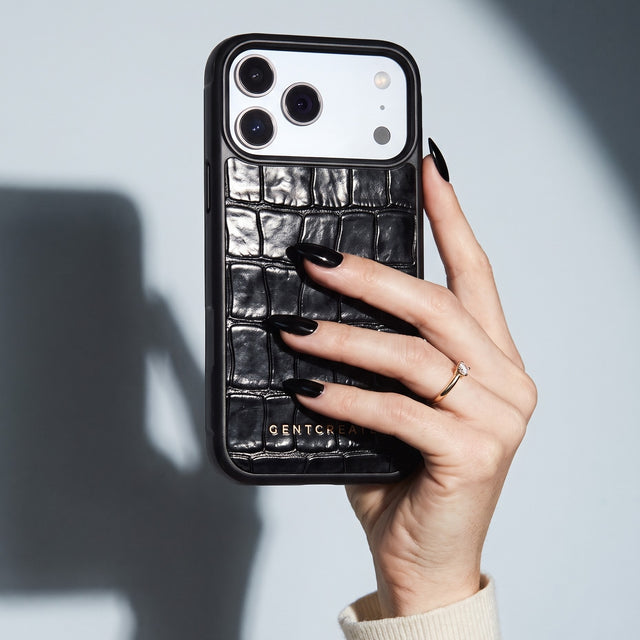 Hand with black nails holding a black glossy crocodile-embossed calfskin iPhone 18 Pro Max case by GENTCREATE