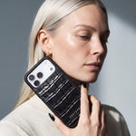 Blonde woman holding a black glossy crocodile-embossed calfskin iPhone 18 Pro Max case by GENTCREATE beside her face