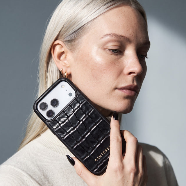 Blonde woman holding a black glossy crocodile-embossed calfskin iPhone 18 Pro Max case by GENTCREATE beside her face