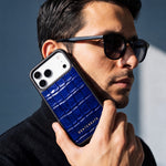 Homme à lunettes de soleil tenant près de son visage une coque iPhone 18 Pro Max GENTCREATE en veau bleu brillant embossé façon crocodile