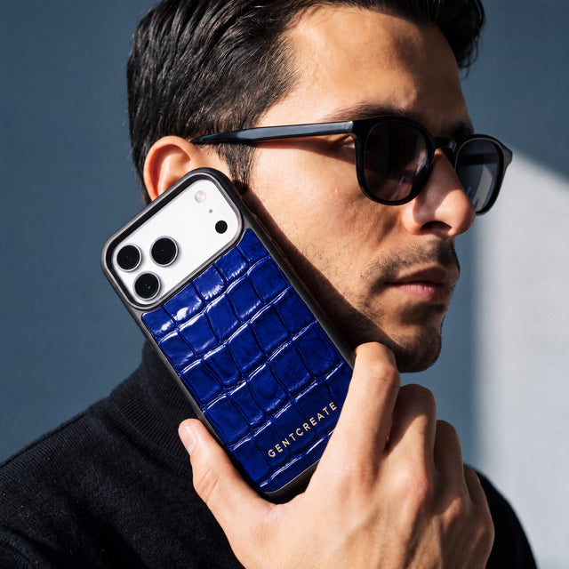 رجل يرتدي نظارة شمسية يمسك جرابًا أزرق لهاتف iPhone 18 Pro Max من جلد عجل لامع بنقش التمساح البارز من GENTCREATE بجانب وجهه