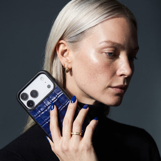 Blonde woman holding a blue glossy crocodile-embossed calfskin iPhone 18 Pro Max case by GENTCREATE beside her face