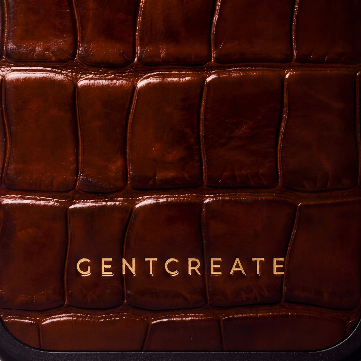 Close-up of the glossy brown crocodile-embossed calfskin and gold GENTCREATE wordmark on an iPhone 18 Pro case