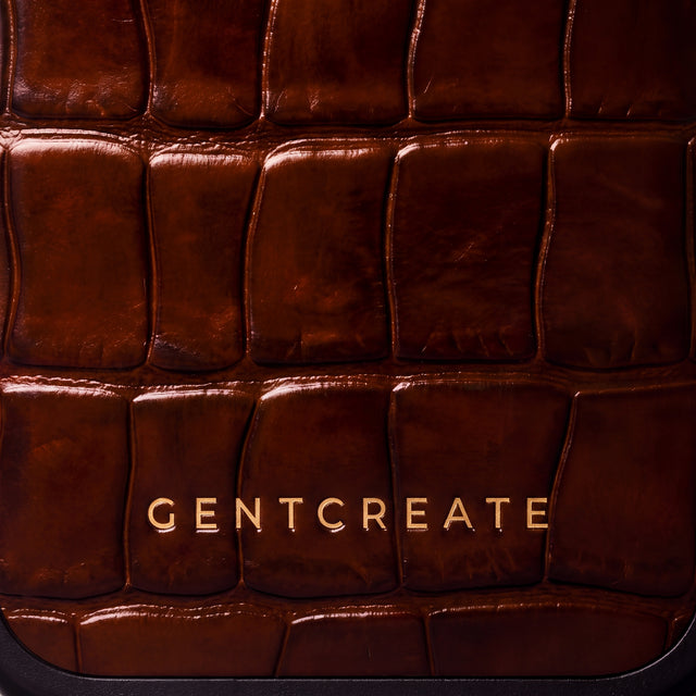 Close-up of the glossy brown crocodile-embossed calfskin and gold GENTCREATE wordmark on an iPhone 18 Pro case