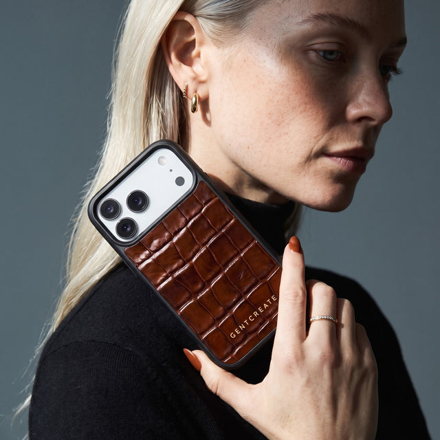 Blonde woman holding a brown glossy crocodile-embossed calfskin iPhone 18 Pro Max case by GENTCREATE beside her face
