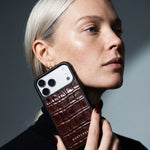Woman holding a burgundy glossy crocodile-embossed calfskin iPhone 18 Pro Max case by GENTCREATE to her cheek
