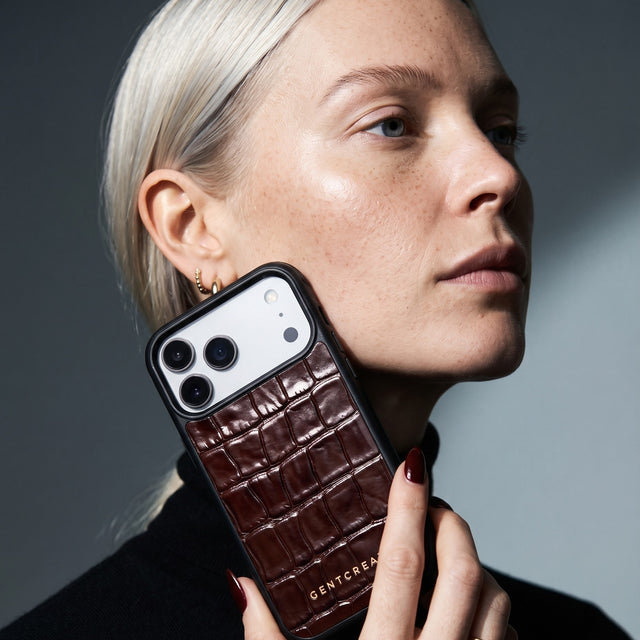 Woman holding a burgundy glossy crocodile-embossed calfskin iPhone 18 Pro Max case by GENTCREATE to her cheek