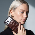Blonde woman holding a burgundy glossy crocodile-embossed calfskin iPhone 18 Pro Max case by GENTCREATE beside her face