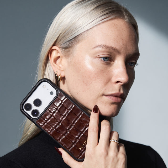 Blonde woman holding a burgundy glossy crocodile-embossed calfskin iPhone 18 Pro Max case by GENTCREATE beside her face