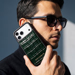 Homme à lunettes de soleil tenant près de son visage une coque iPhone 18 Pro Max GENTCREATE en veau vert brillant embossé façon crocodile