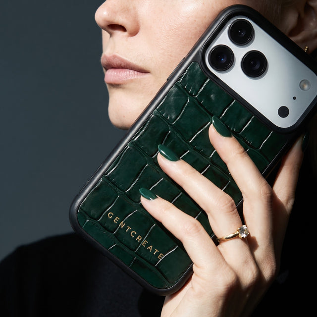 Woman holding a green glossy crocodile-embossed calfskin iPhone 18 Pro Max case by GENTCREATE against her jaw