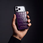 Man's hand holding a magenta glossy crocodile-embossed calfskin iPhone 18 Pro Max case by GENTCREATE in a dark studio