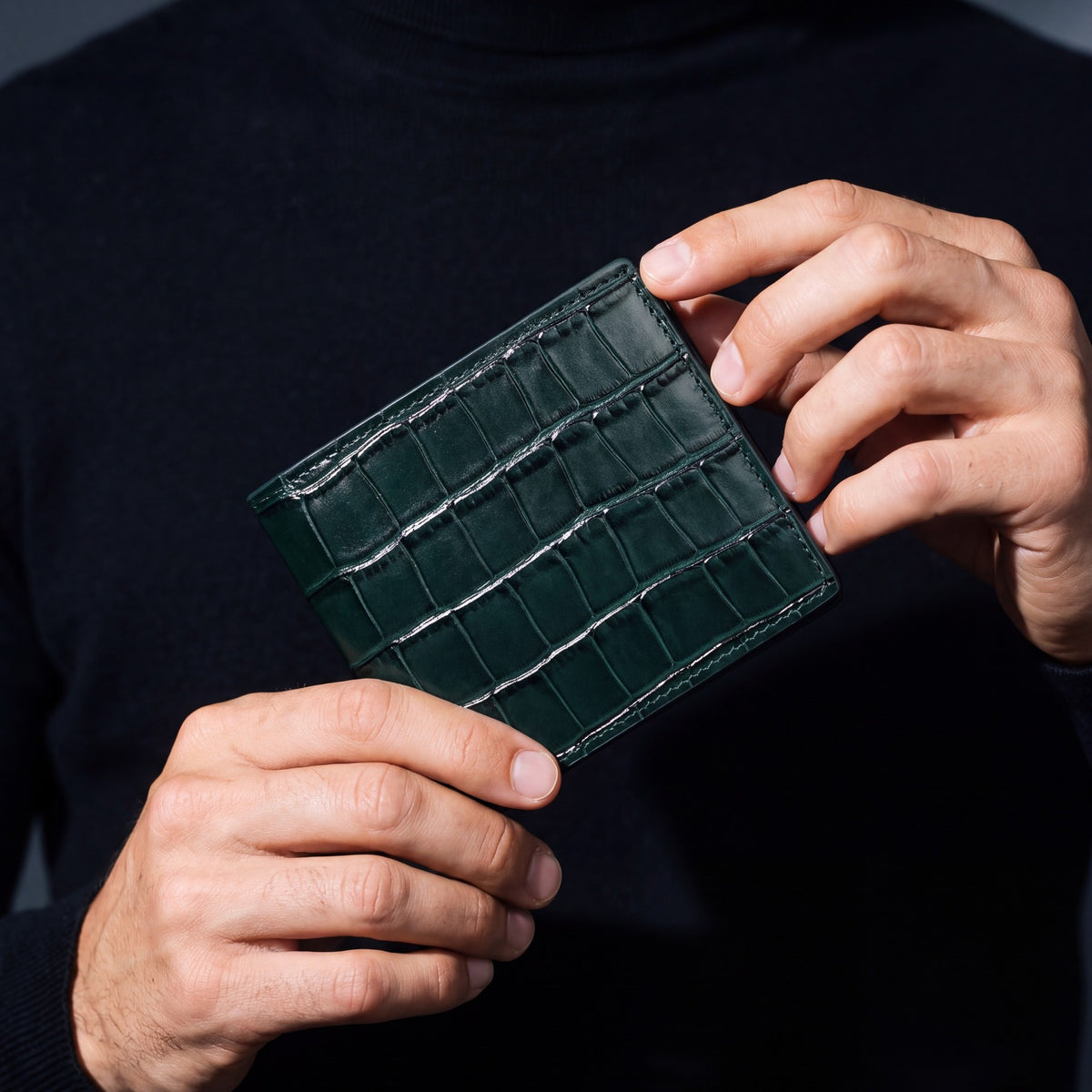 Close-up of hands holding a green crocodile-embossed leather bifold wallet by GENTCREATE