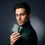 Man holding a green crocodile-embossed leather bifold wallet by GENTCREATE up over the shoulder