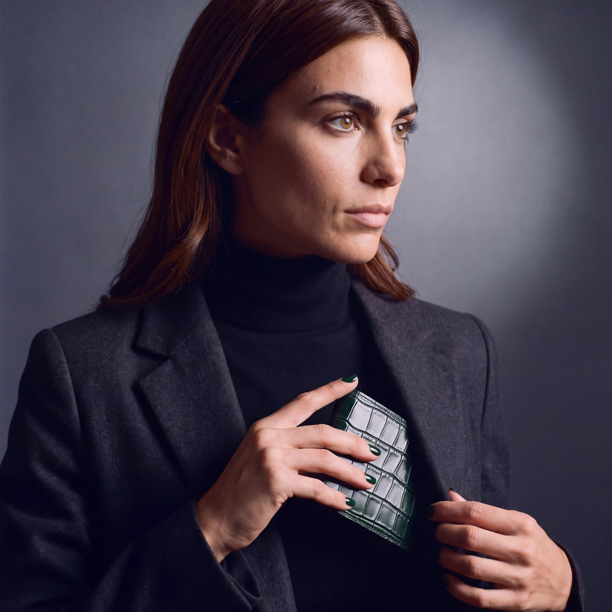 Woman sliding a green crocodile-embossed leather bifold wallet by GENTCREATE into a blazer pocket