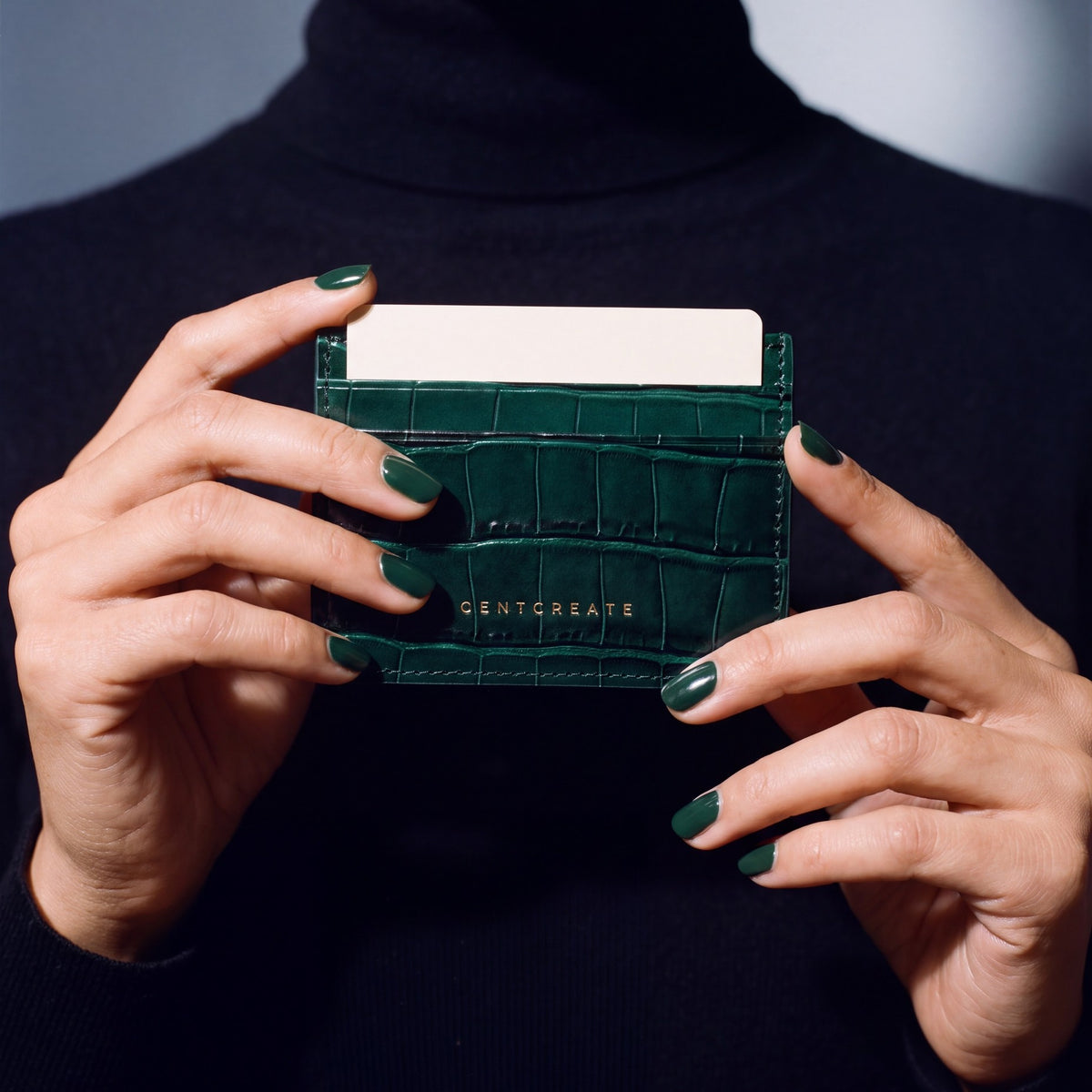 Close-up of hands holding a green crocodile-embossed leather card holder by GENTCREATE with a card in the top slot