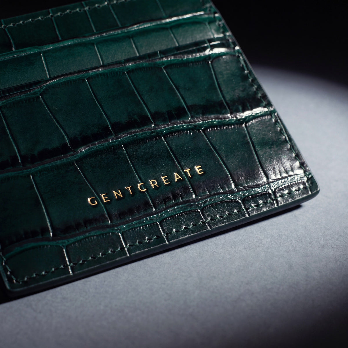 Close-up of the gold GENTCREATE stamp pressed into a green crocodile-embossed leather card holder