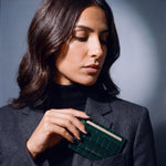Woman slipping a green crocodile-embossed leather card holder by GENTCREATE into a blazer chest pocket