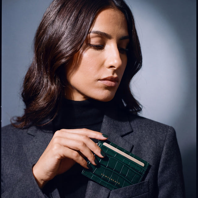 Woman slipping a green crocodile-embossed leather card holder by GENTCREATE into a blazer chest pocket