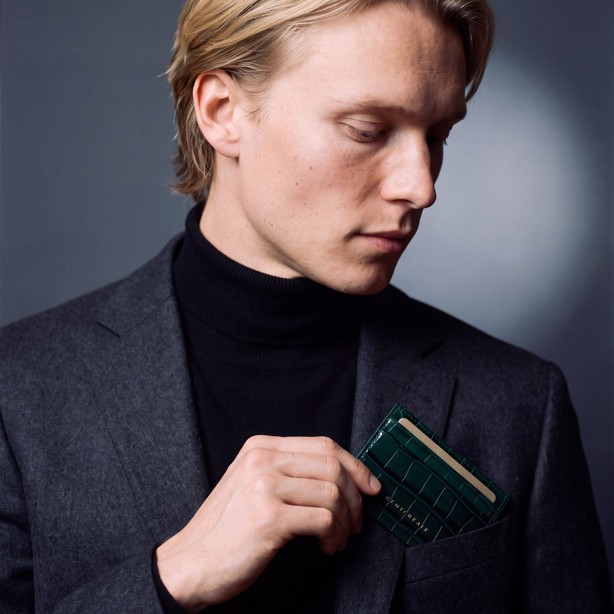 Man slipping a green crocodile-embossed leather card holder by GENTCREATE into a blazer chest pocket