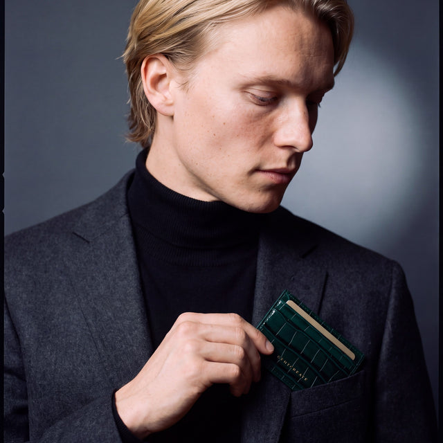 Man slipping a green crocodile-embossed leather card holder by GENTCREATE into a blazer chest pocket