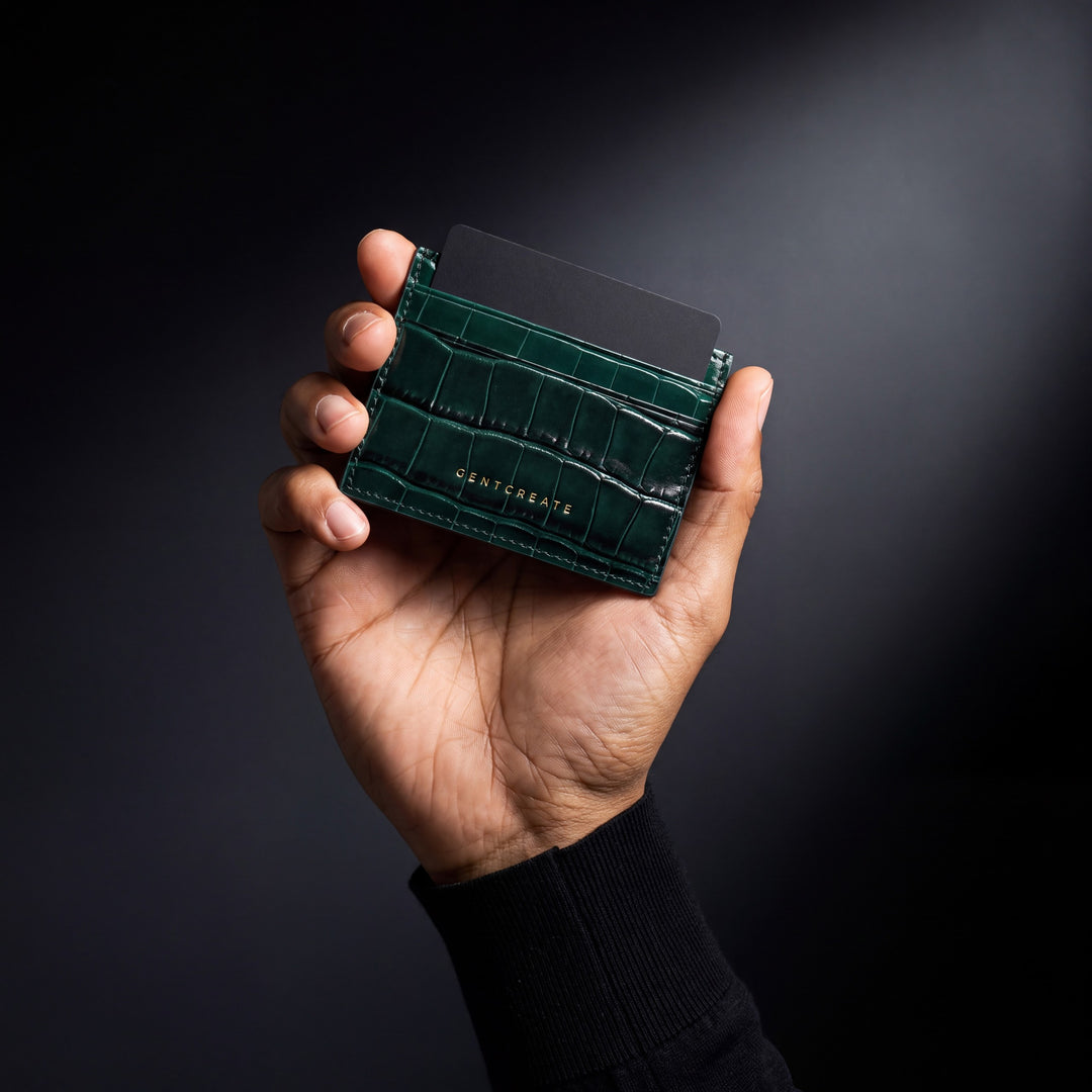 A hand holds a green crocodile-embossed GENTCREATE card holder with a card in it