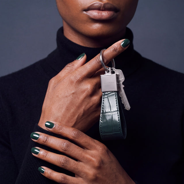 Close-up of a green crocodile-embossed leather keychain by GENTCREATE with house keys hanging from a finger