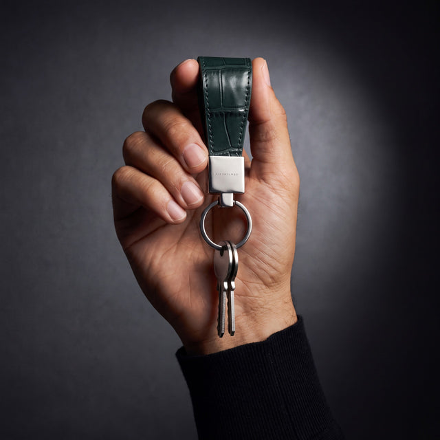 Man's hand holding up a green crocodile-embossed leather keychain by GENTCREATE with keys in a dark studio