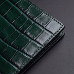 Gros plan sur les écailles brillantes du motif crocodile embossé et le bord cousu d'un portefeuille GENTCREATE à deux volets en cuir vert