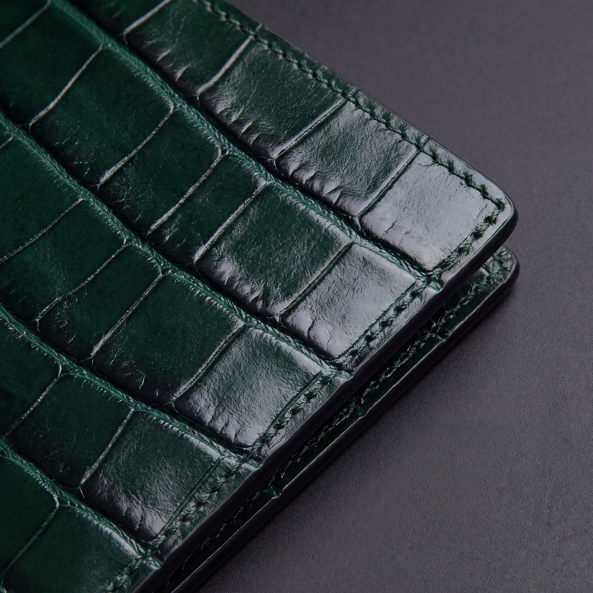 Gros plan sur les écailles brillantes du motif crocodile embossé et le bord cousu d'un portefeuille GENTCREATE à deux volets en cuir vert