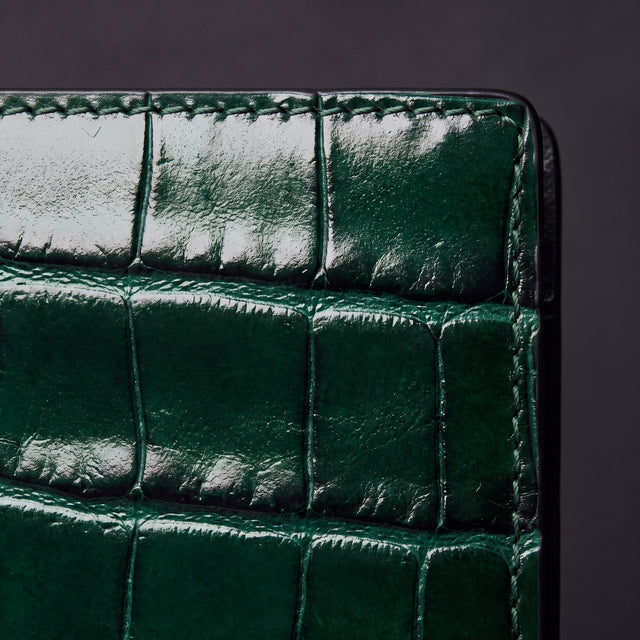 Grande plano das escamas brilhantes em relevo efeito croco e do rebordo cosido de um porta-passaporte verde da GENTCREATE