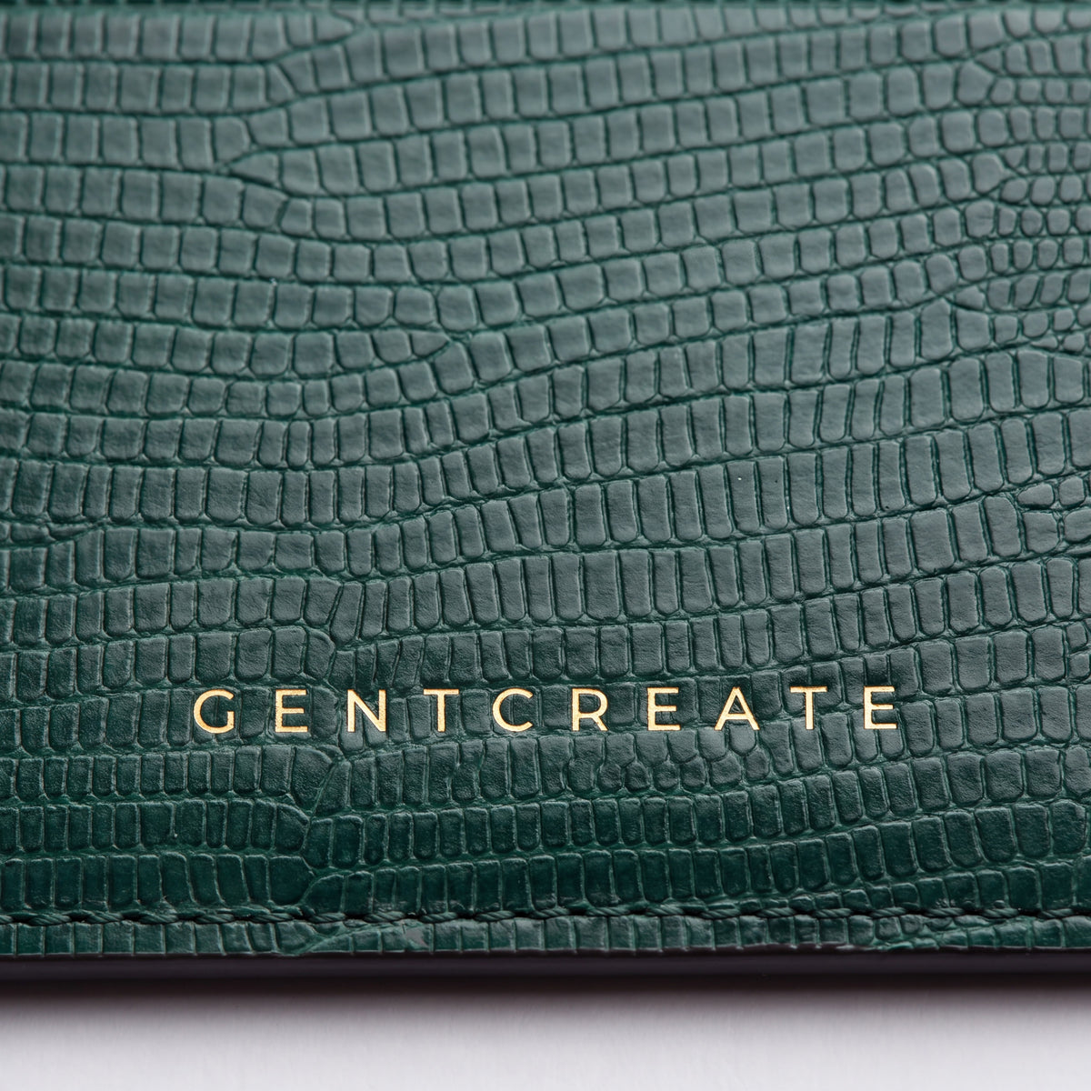 Close-up of the gold GENTCREATE stamp on a green lizard-embossed leather card holder