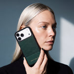Mujer sosteniendo contra la mejilla una funda verde de GENTCREATE para iPhone 18 Pro Max en piel de ternera con grabado de lagarto, a la luz de una ventana