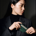 Woman slipping a green pebble leather card holder by GENTCREATE into a blazer chest pocket
