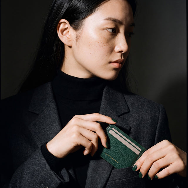 Woman slipping a green pebble leather card holder by GENTCREATE into a blazer chest pocket