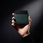 இருண்ட ஸ்டுடியோவில் ஒரு கார்டுடன் கூடிய GENTCREATE பச்சை நிறக் கூழாங்கல் அமைப்புத் தோல் கார்டு ஹோல்டரைப் பிடித்திருக்கும் பெண்ணின் கை