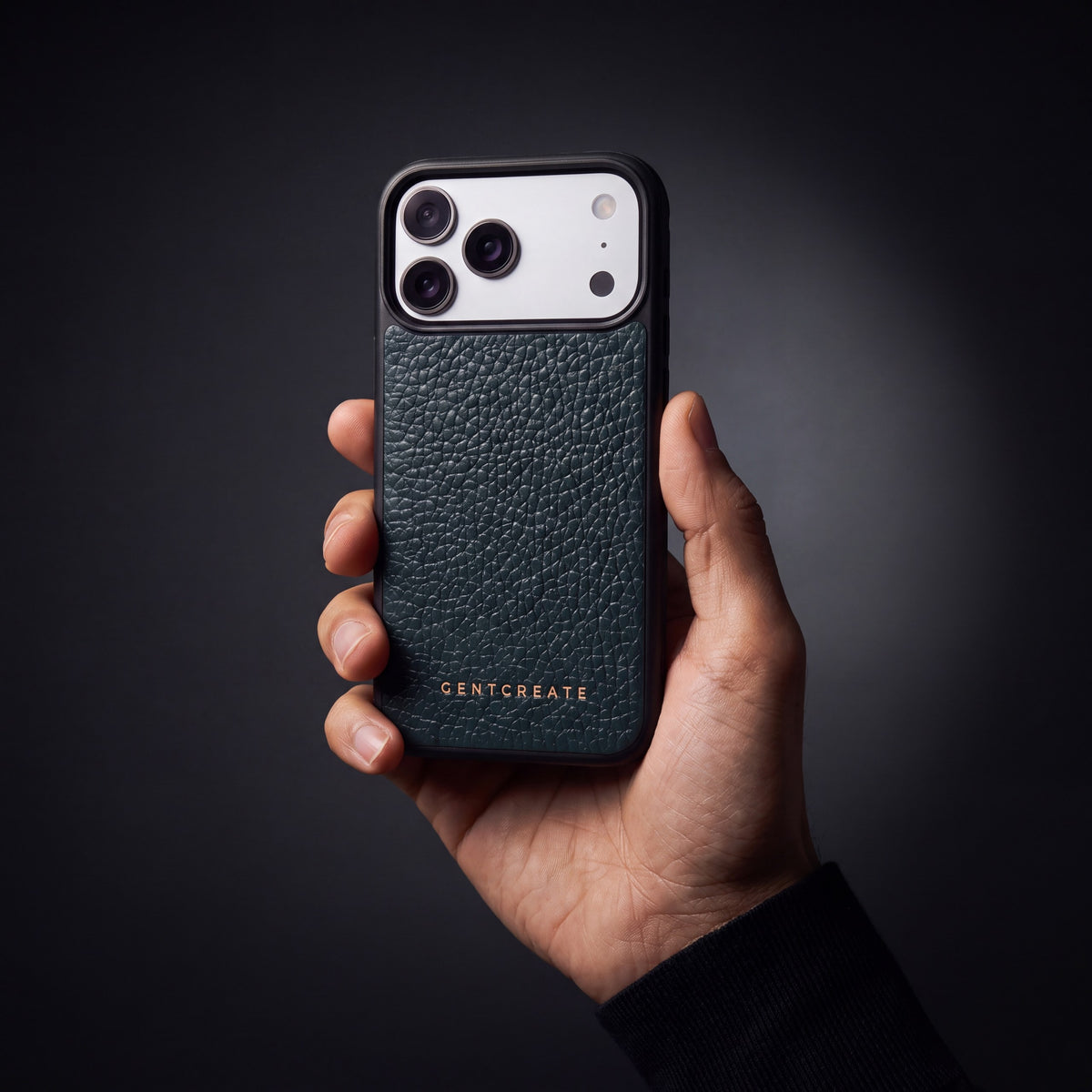 Man's hand holding a green pebble-grain calfskin iPhone 18 Pro Max case by GENTCREATE in a dark studio