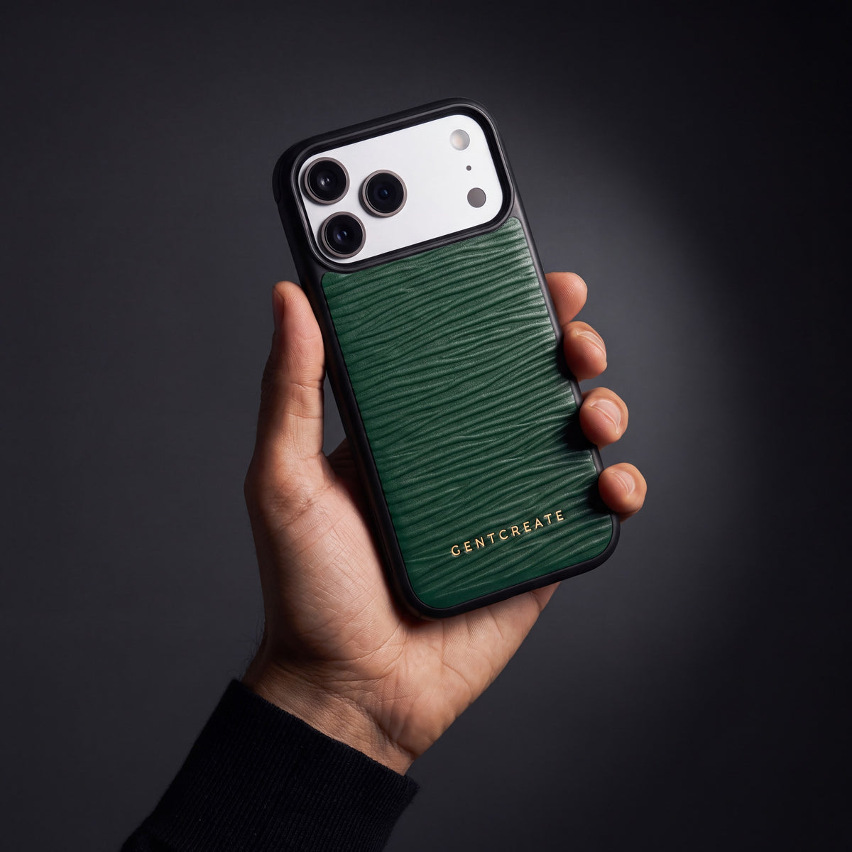 يد رجل تمسك جراب أخضر لهاتف iPhone 18 Pro Max من جلد عجل بنقش موجي بارز من GENTCREATE في استوديو مظلم