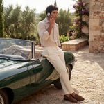 Man holding the GENTCREATE pebble leather iPhone case and leaning on a classic green convertible car in a scenic outdoor setting.