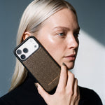 Kvinde holder et kaki iPhone 18 Pro Max-cover i narvet kalveskind fra GENTCREATE ind mod kinden i dagslys fra et vindue