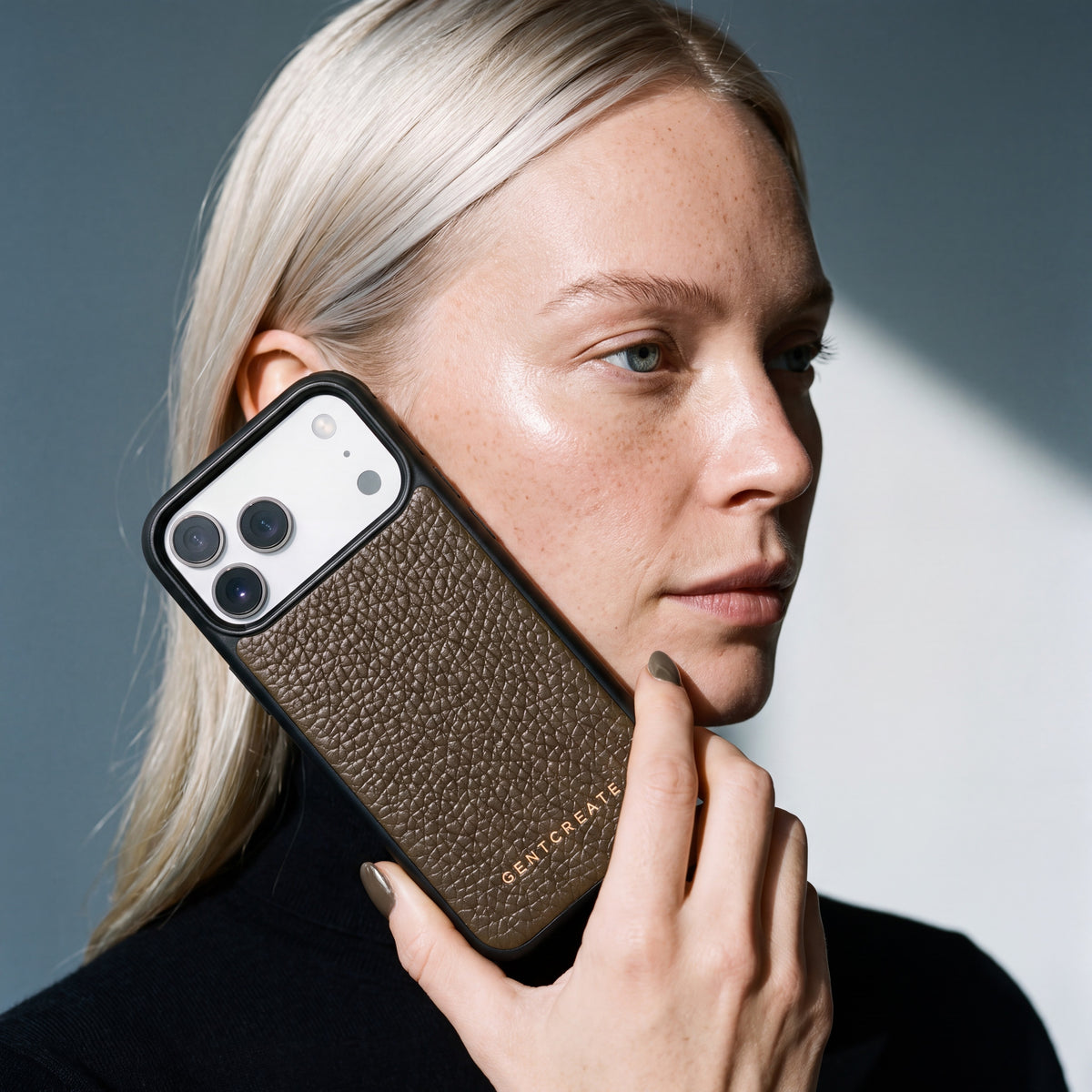 Kvinde holder et kaki iPhone 18 Pro Max-cover i narvet kalveskind fra GENTCREATE ind mod kinden i dagslys fra et vindue