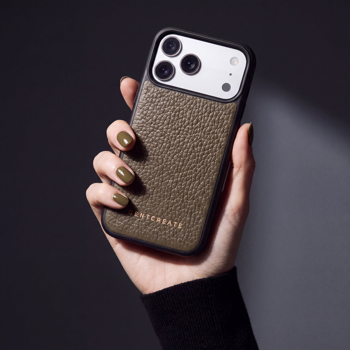 Hand with olive-khaki nails holding a khaki pebble-grain calfskin iPhone 18 Pro Max case by GENTCREATE