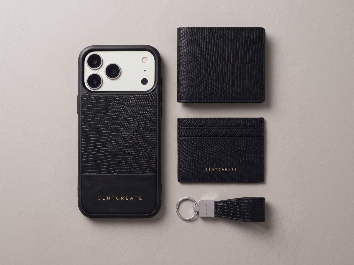 Visualisointi: GENTCREATE-nahkasetti päivänä 1 mustaa liskokuvioitua vasikannahkaa: iPhone-kuori, taitettava lompakko, korttikotelo ja avaimenperä vaalealla kivellä.