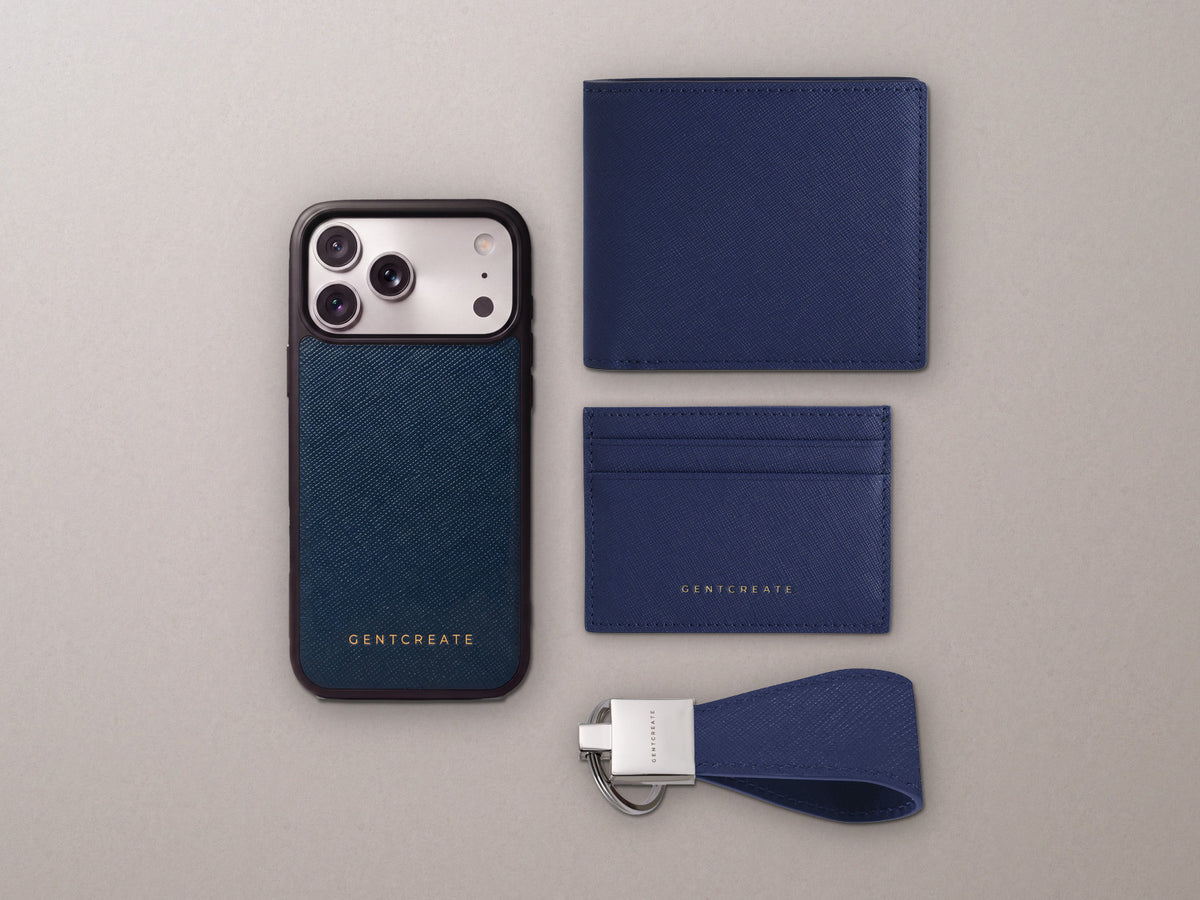 Visualisointi: GENTCREATE-nahkasetti päivänä 1 laivastonsinistä ristikuvioitua Saffiano-vasikannahkaa: iPhone-kuori, taitettava lompakko, korttikotelo ja avaimenperä vaalealla kivellä.