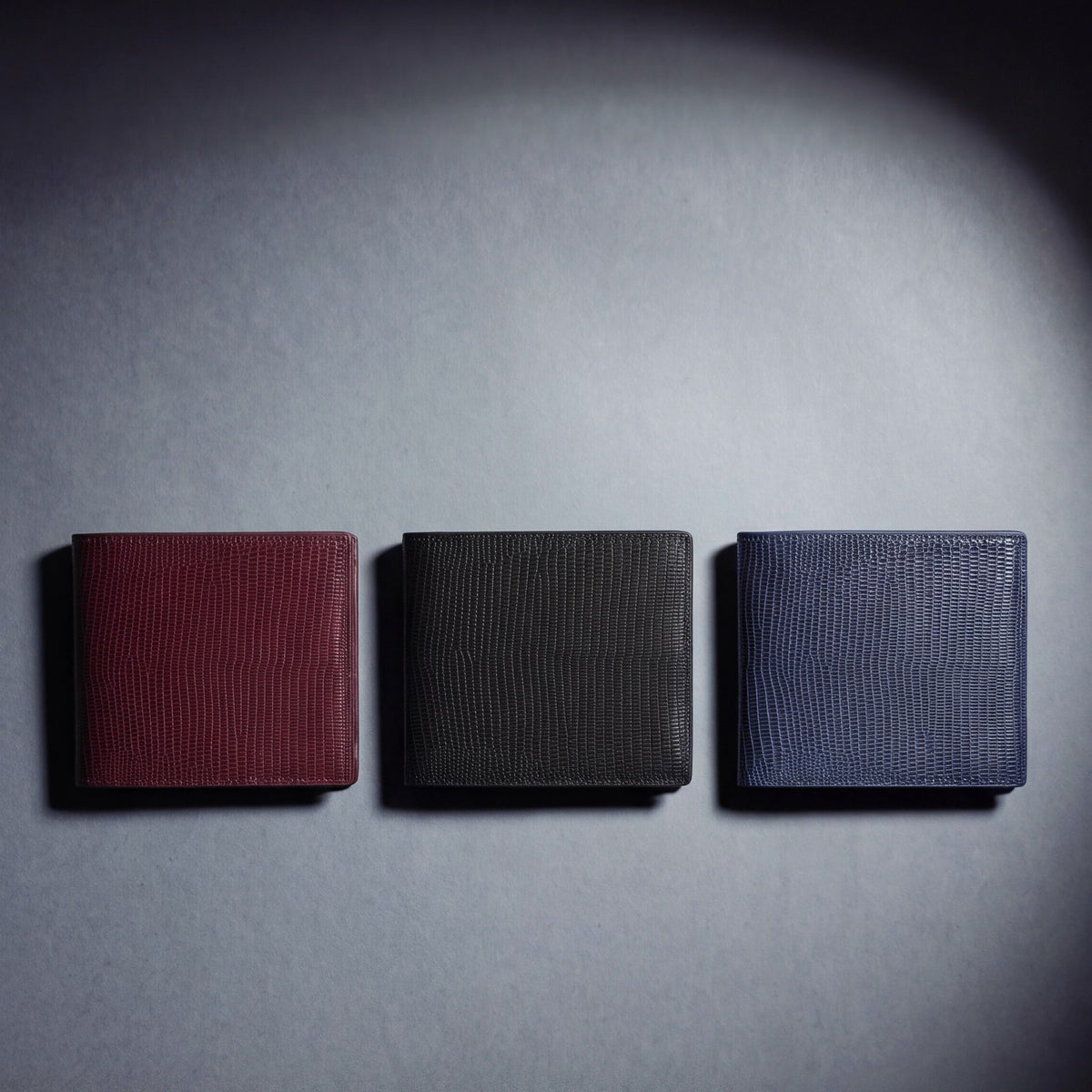 Lizard-embossed leather bifold wallet by GENTCREATE in burgundy, black and navy, laid flat