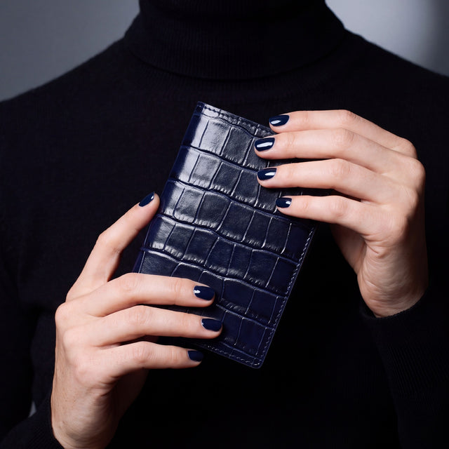 Close-up of hands holding a navy crocodile-embossed leather passport holder by GENTCREATE