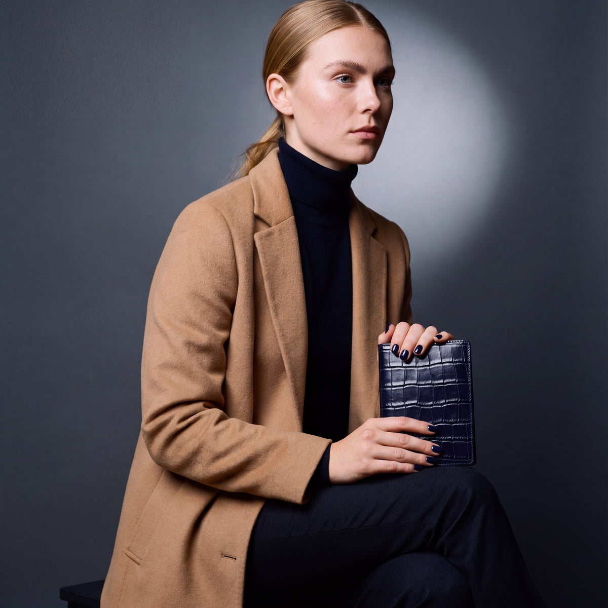 Woman seated, holding a navy crocodile-embossed leather passport holder by GENTCREATE